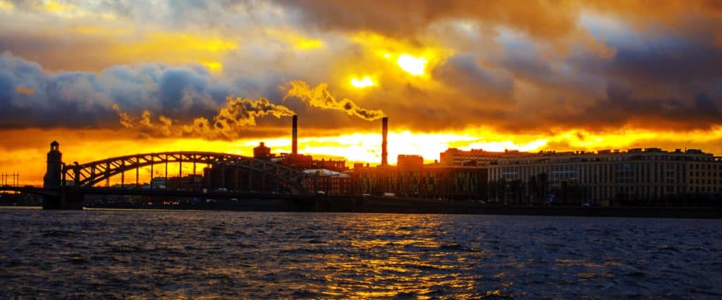 Golden sky sunset image of a bridge and large body of water with buildings on the shoreline