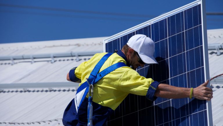 Man carrying solar panel wearing harness and high visibility yellow shirt