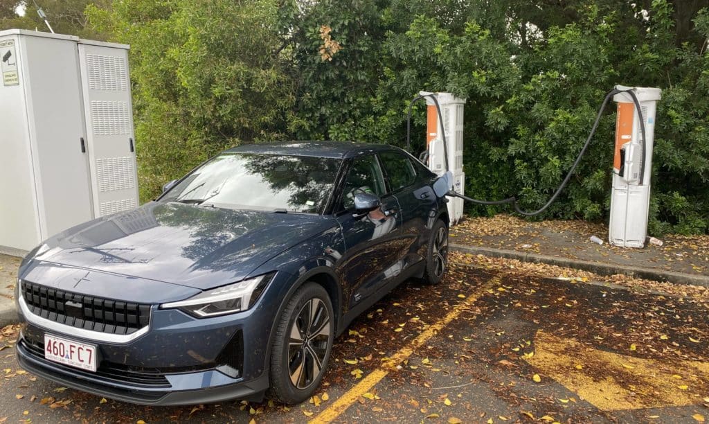 Dark blue sedan parked in a parking bay with an EV charger plugged in at the rear